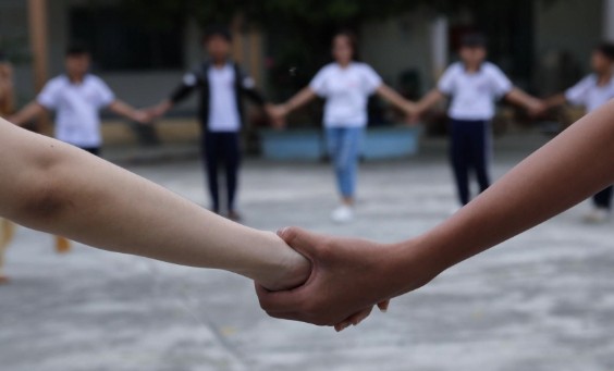Young adults gather in a circle holding hands at a community event.